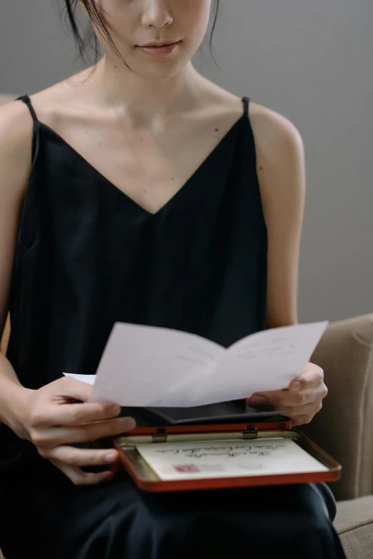 a woman sitting on a couch reading a book, an album cover, by Ruth Jên, pexels contest winner, romanticism, wearing black camisole outfit, pen and paper, upper body close - up, standing