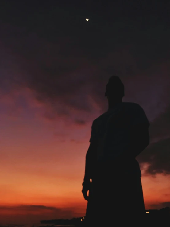 a man standing on top of a beach next to the ocean, pexels contest winner, silhouette over sunset, ☁🌪🌙👩🏾, profile posing, moody aesthetic