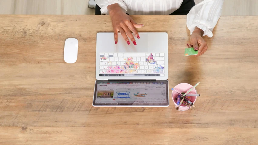 a woman sitting at a desk using a laptop computer, trending on pexels, process art, floral patterned skin, on a wooden desk, multi - coloured, white backround