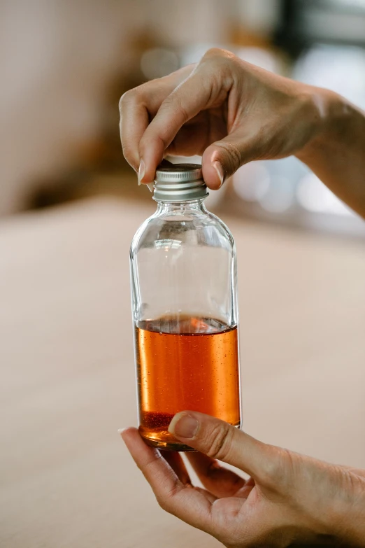 a close up of a person holding a bottle of liquid, by Jessie Algie, unsplash, cinnamon skin color, prototype, whiskey bottle, drinking cough syrup