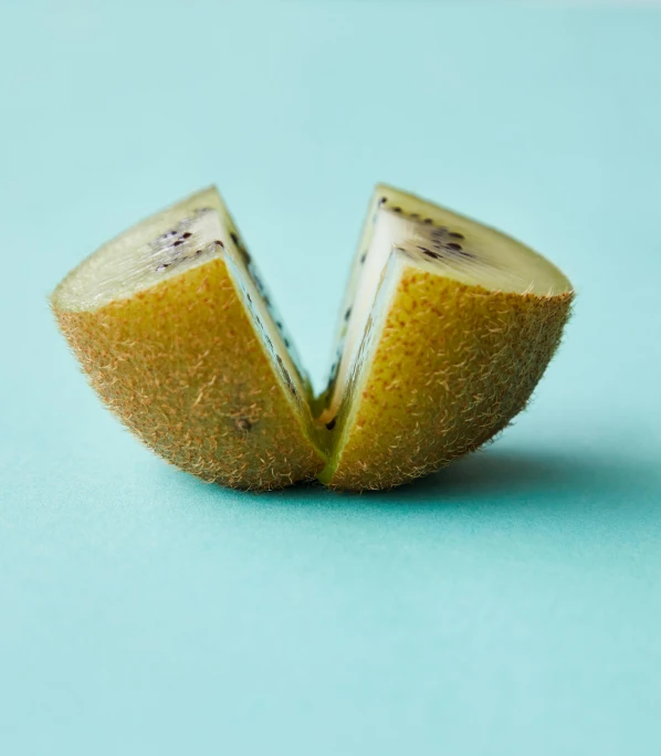 a kiwi cut in half on a blue surface, by Elsa Bleda, unsplash, berries inside structure, shot on hasselblad, pear for a head, taken in the early 2020s