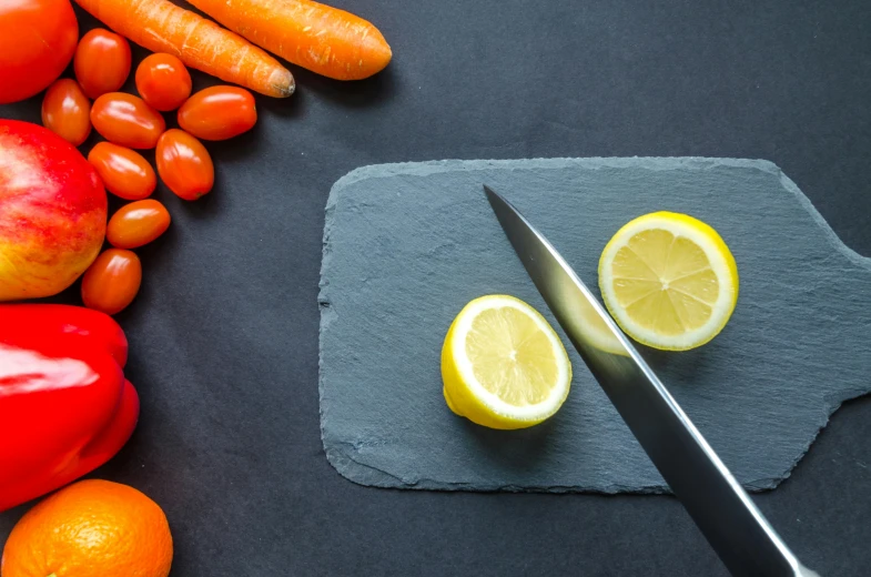 a knife sitting on top of a cutting board next to fruit and vegetables, slate, thumbnail, carrot, no cropping