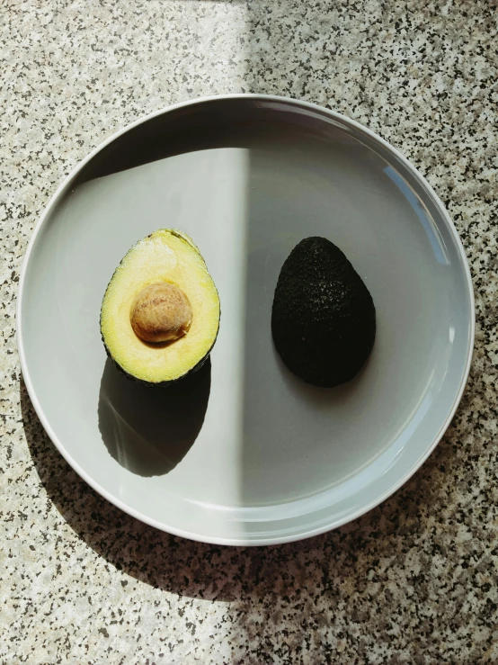 an avocado cut in half on a plate, inspired by René Magritte, trending on unsplash, hyperrealism, grey, arranged in the golden ratio, symmetric balance), yinyang shaped