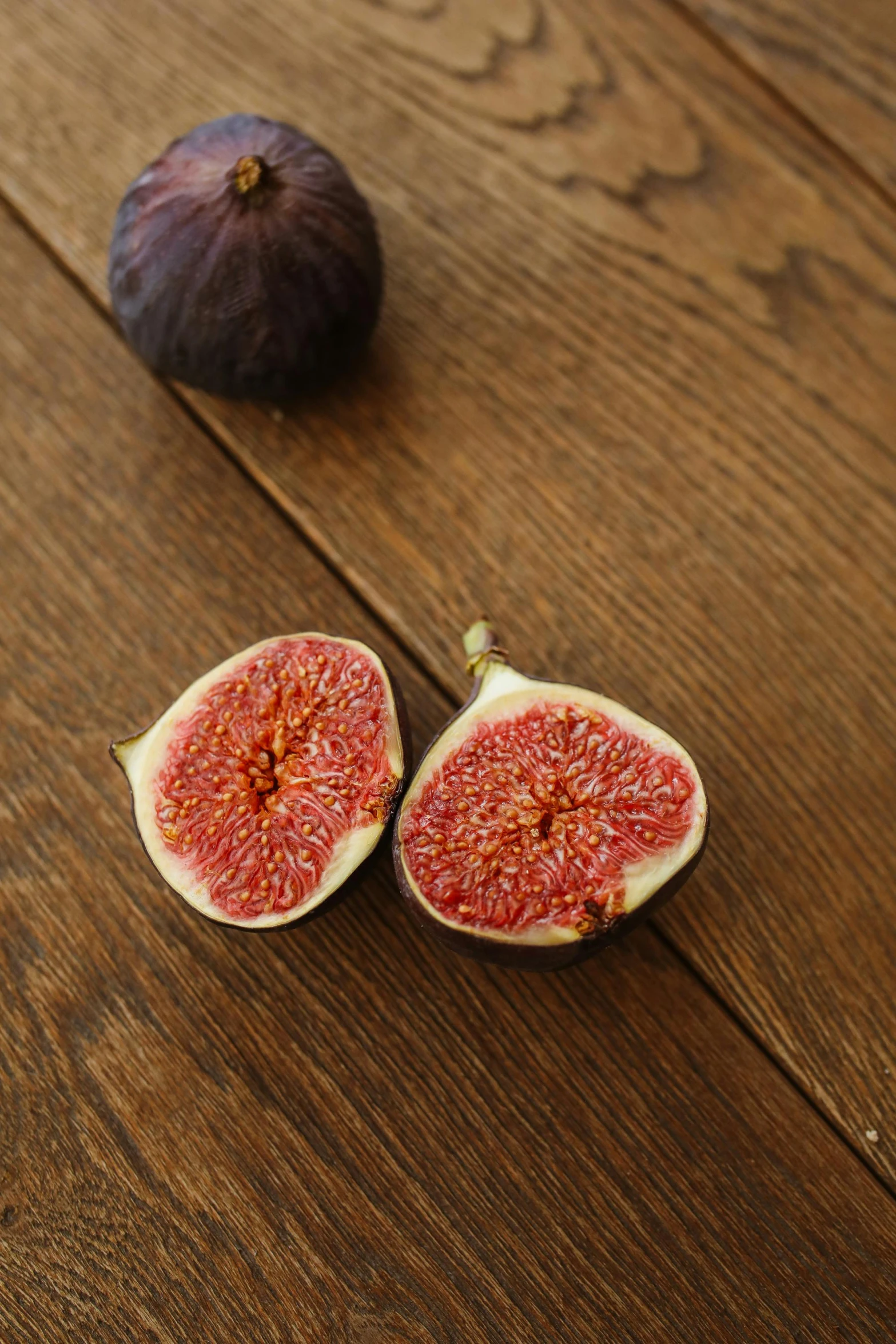 a couple of figs sitting on top of a wooden table, back facing the camera, puce and vermillion, ballard, medium format