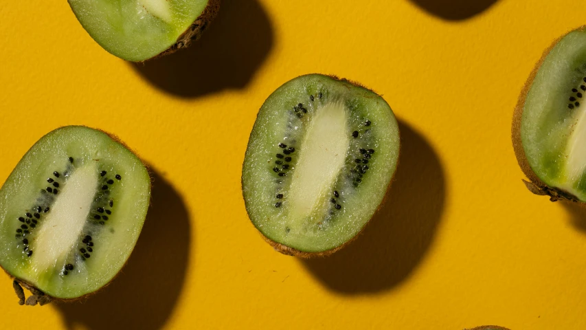 a group of kiwis cut in half on a yellow surface, by Carey Morris, trending on pexels, hurufiyya, berries inside structure, green, 🐿🍸🍋, close - up face