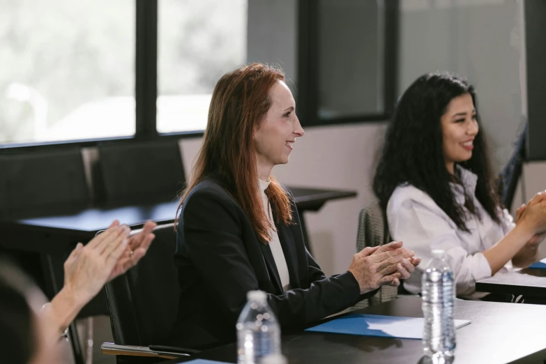 a group of people sitting at a table clapping, a portrait, unsplash, woman in business suit, background image, colour photograph, wide shot photograph