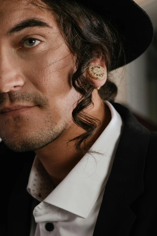 a close up of a person wearing a hat, an album cover, inspired by Jules Robert Auguste, masculine jawline, earring, jörmungandr, liberty curls