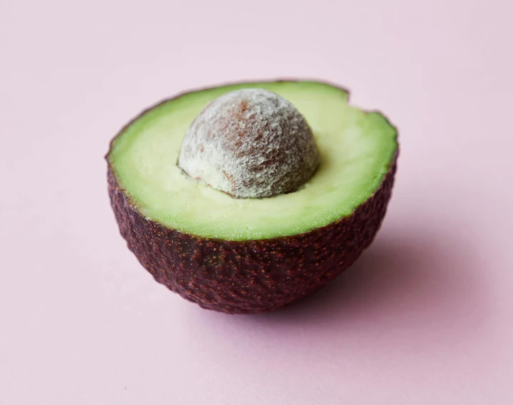 an avocado cut in half on a pink surface, trending on pexels, halo halo halo halo 8k, weathered olive skin, shot on hasselblad, grey