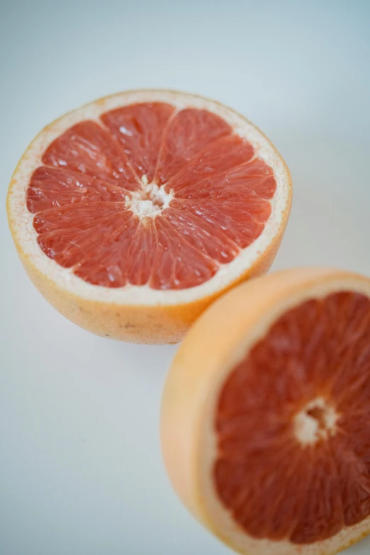 two grapefruits cut in half on a white surface, by Julian Allen, unsplash, made of glazed, close up details, alabama, lots of details