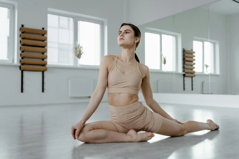 a woman sitting on the floor in a yoga pose, a picture, by Emma Andijewska, trending on pexels, arabesque, bare midriff, sculpting, light tan, low quality photo