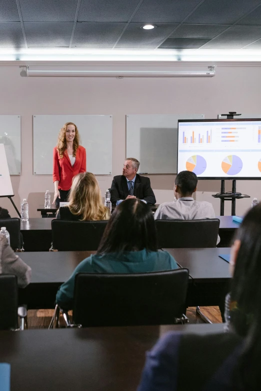 a woman giving a presentation to a group of people, by Gavin Hamilton, trending on unsplash, academic art, graded with davinci resolve, inspect in inventory image, classroom in background, wide shot 4k result