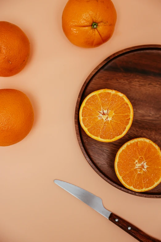 a wooden plate topped with oranges next to a knife, trending on pexels, essence, ilustration, round format, organics