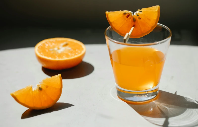 a glass of orange juice sitting on top of a table, trending on pexels, grey orange, background image, spirits, various posed