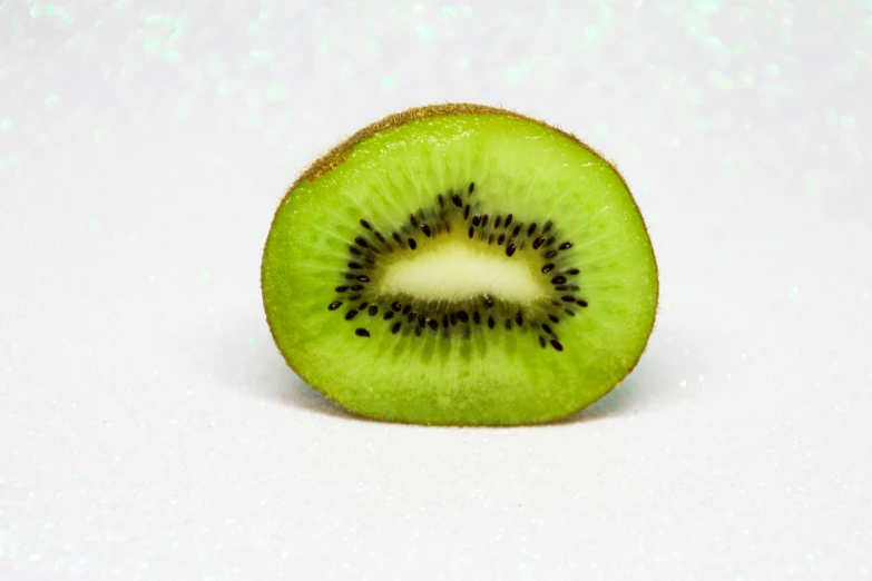 a kiwi cut in half on a white surface, by Gavin Hamilton, trending on unsplash, green sparkles, 2000s photo, neon green, in front of white back drop