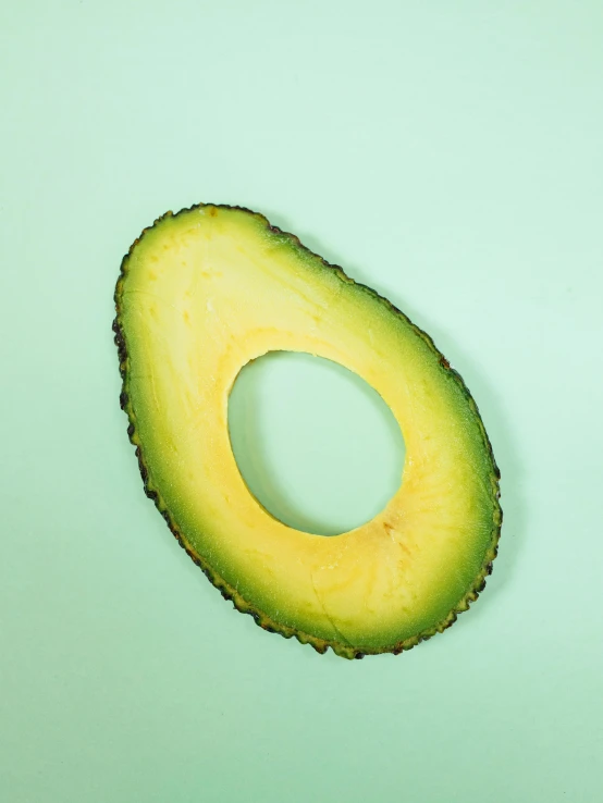 an avocado cut in half on a green surface, an album cover, trending on pexels, detailed product image, organic shape, natural soft rim light, on yellow paper