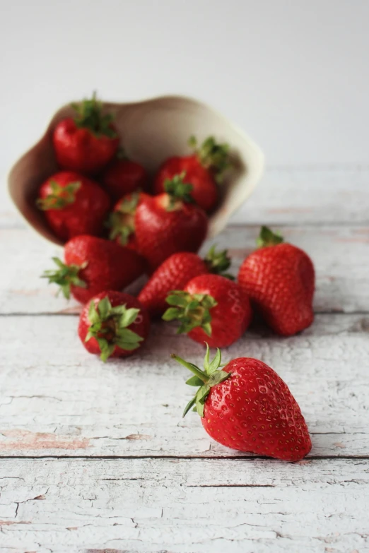 a bowl of strawberries sitting on top of a wooden table