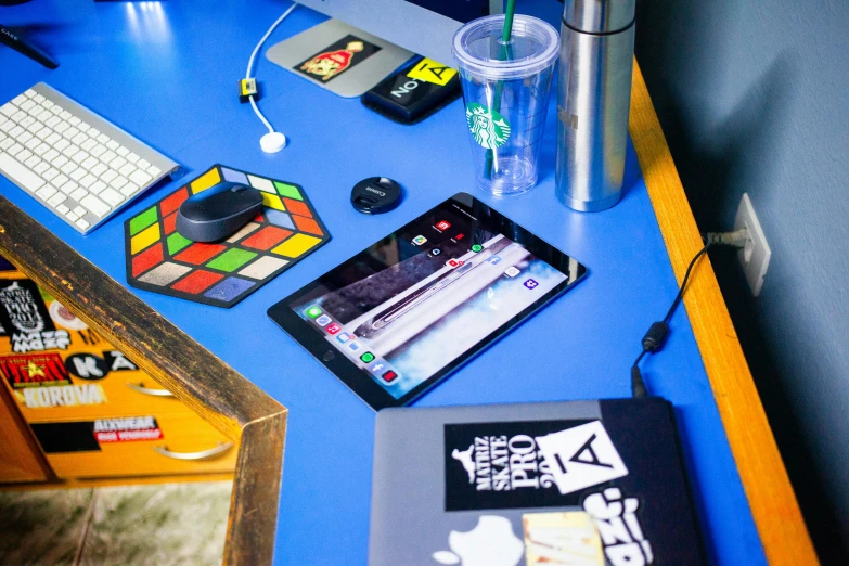 a laptop computer sitting on top of a blue desk, board games on a table, small hipster coffee shop, ipad pro, a rubik's cube