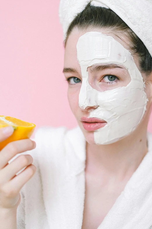 a woman holding a slice of orange in front of her face, trending on pexels, renaissance, white mask, pink face, candy treatments, square