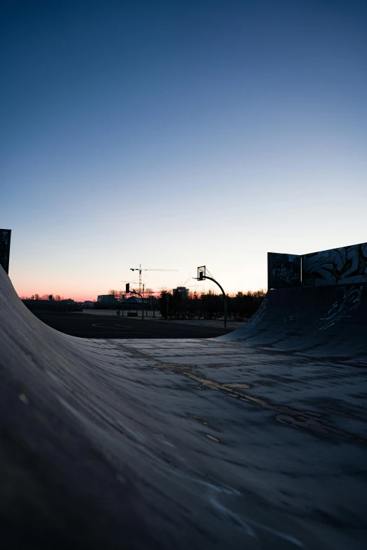 a man riding a skateboard up the side of a ramp, a picture, by Tom Bonson, unsplash contest winner, graffiti, dusk sky, helsinki, wide field of view, curved