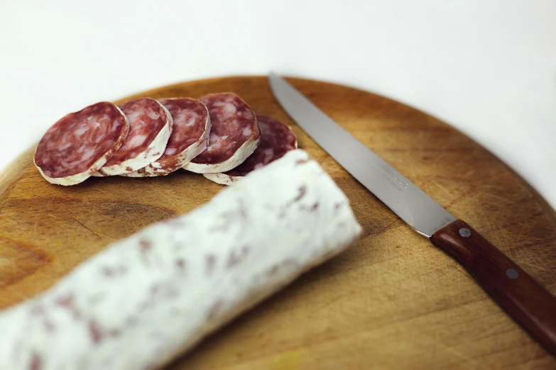 a piece of meat sitting on top of a cutting board next to a knife, arabesque, holding a baguette, cream, salami, petite