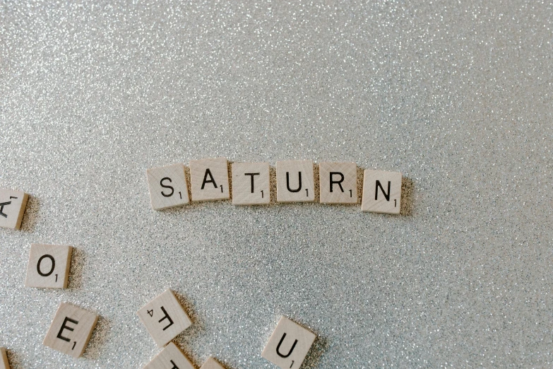 the word saturn spelled with scrabbles on a metallic surface, by Sara Saftleven, trending on unsplash, letterism, 🌲🌌, stardust, douglas adams, white