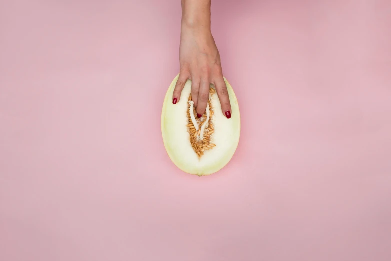 a woman's hand holding a cantaloupe on a pink background, by Julia Pishtar, trending on pexels, magic realism, gold body, clemens ascher, selena gomez made out of celery, 🍸🍋