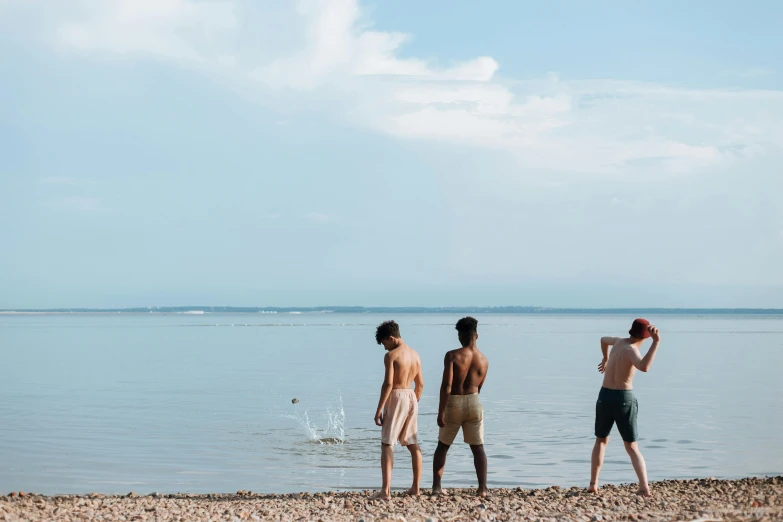 a group of men standing on top of a beach next to a body of water, by Attila Meszlenyi, unsplash, figuration libre, kids playing, photograph of three ravers, still from a wes anderson film, teenage boy