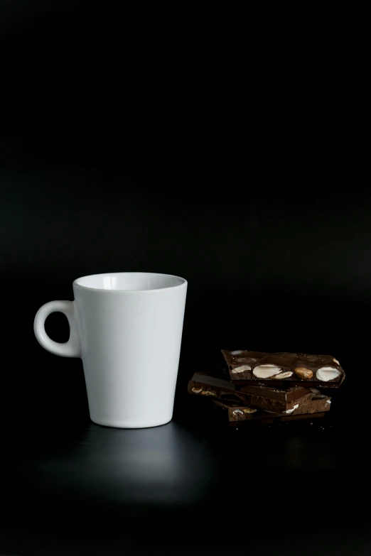 a white cup sitting next to a piece of chocolate, inspired by Gillis Rombouts, ultrawide image, hero shot, square, nut