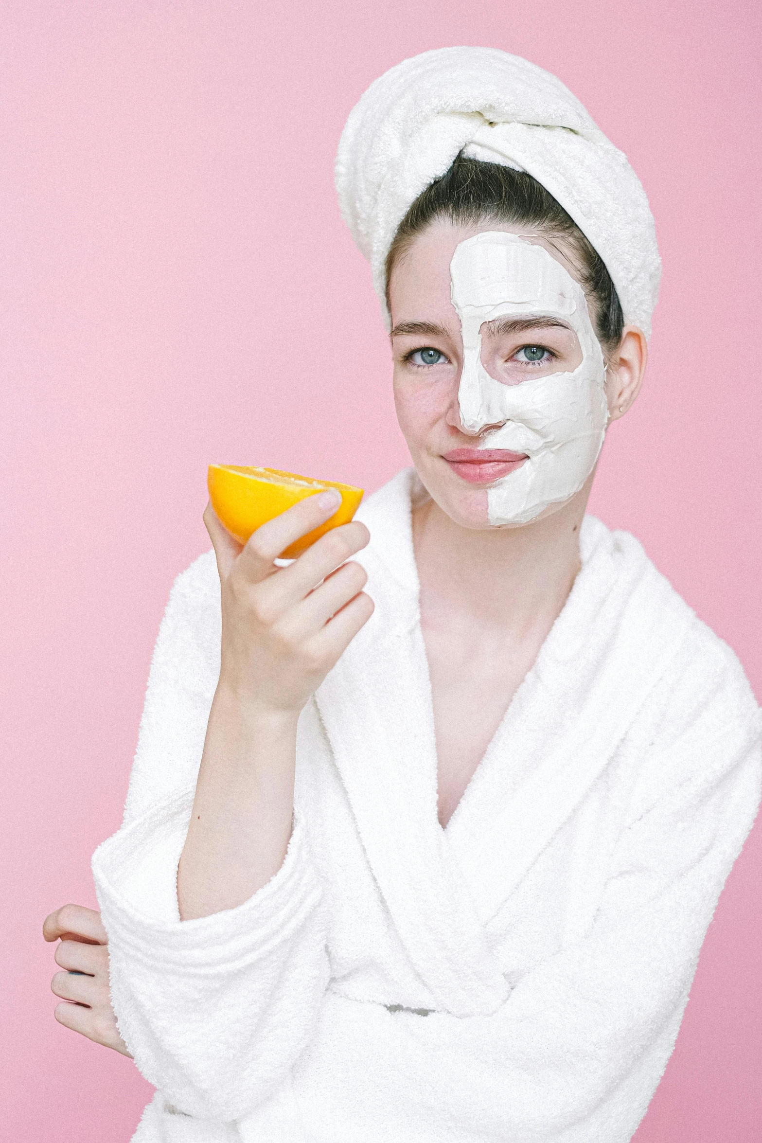 a woman in a bathrobe holding an orange, trending on pexels, white face paint, banana, pink face, masking