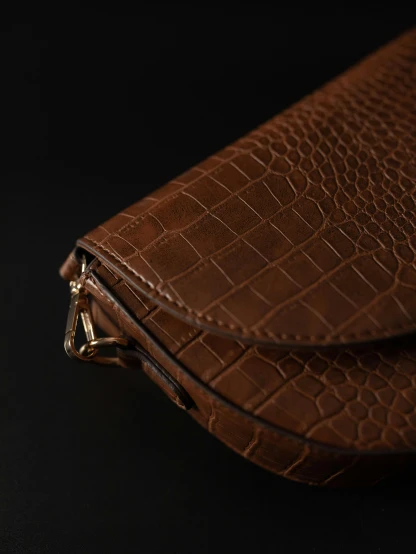 a brown purse sitting on top of a black table, by Nina Hamnett, trending on unsplash, side view intricate details, curved. studio lighting, half crocodile, high detailed print