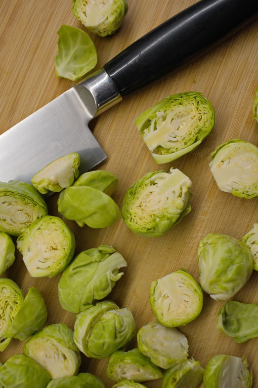 a knife sitting on top of a cutting board next to a pile of brussels sprouts, petite, 3 4 5 3 1, green