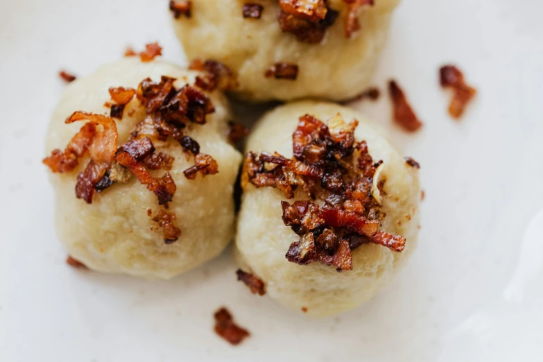 a white plate topped with three doughnuts covered in bacon, by Emma Andijewska, unsplash, baroque, dumplings on a plate, closeup detailed, puffballs, cheesy