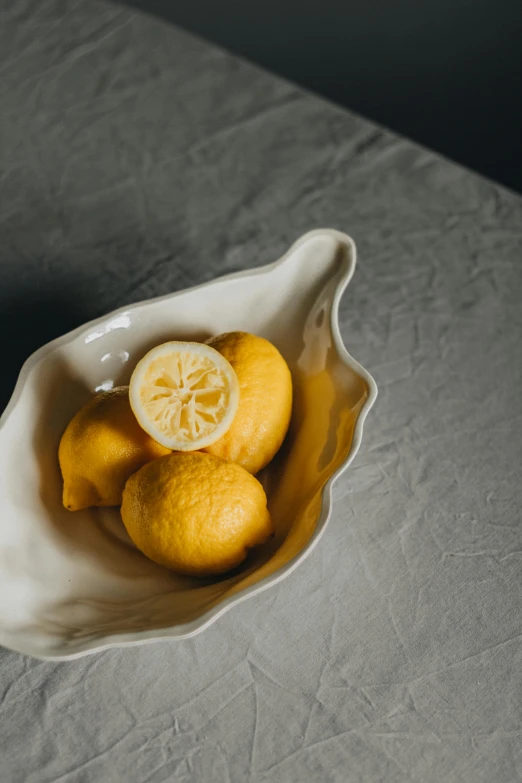 a white bowl filled with lemons on top of a table, inspired by Li Di, unsplash, renaissance, award-winning crisp details”, large shell, curved, serving body