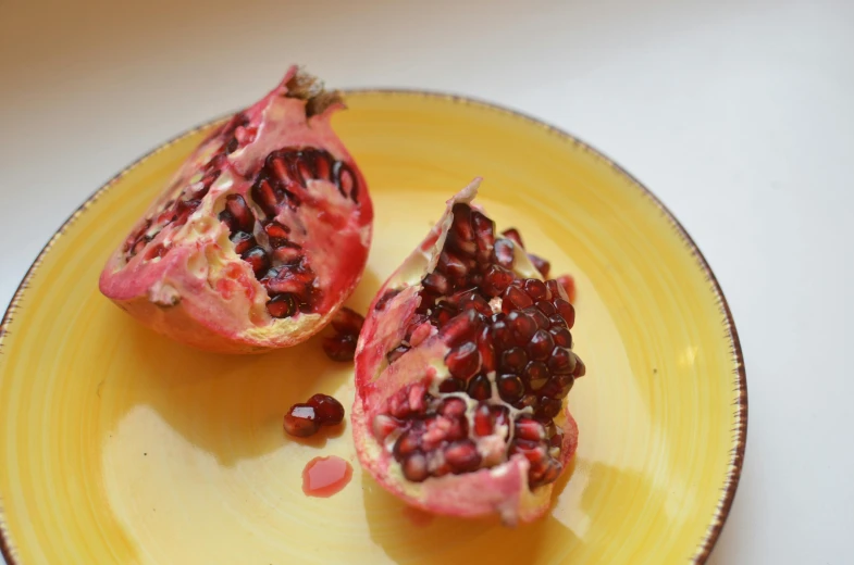 a yellow plate topped with a cut open pomegranate, by Lorraine Fox, pexels, with a whitish, skin, pink, seeds