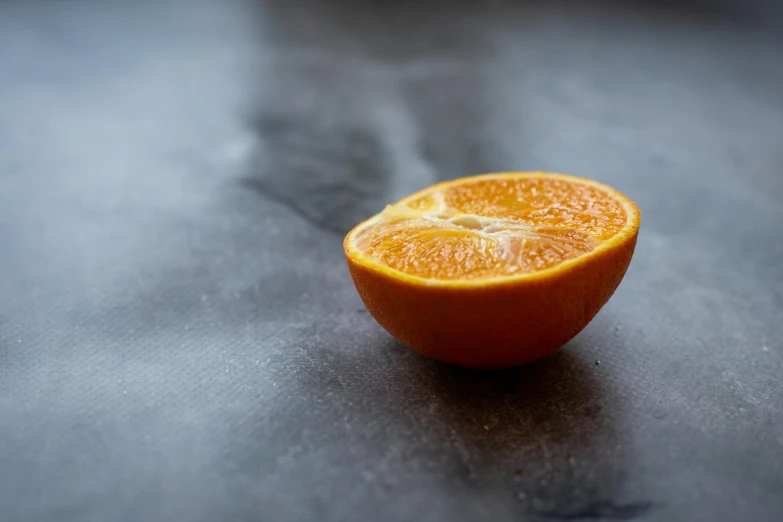 a half of an orange sitting on a table, on a gray background, background image, less detailing, no watermarks