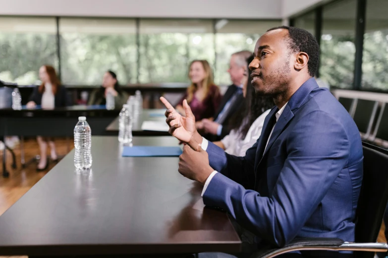 a man sitting at a table in front of a group of people, professional image, diverse, realistic »