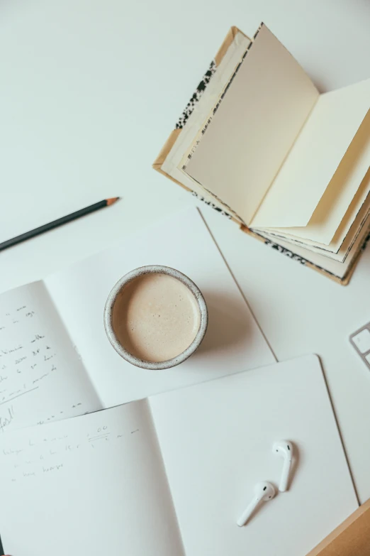 an open book sitting on top of a table next to a cup of coffee, a drawing, trending on unsplash, cream and white color scheme, 9 9 designs, white studio, a high angle shot