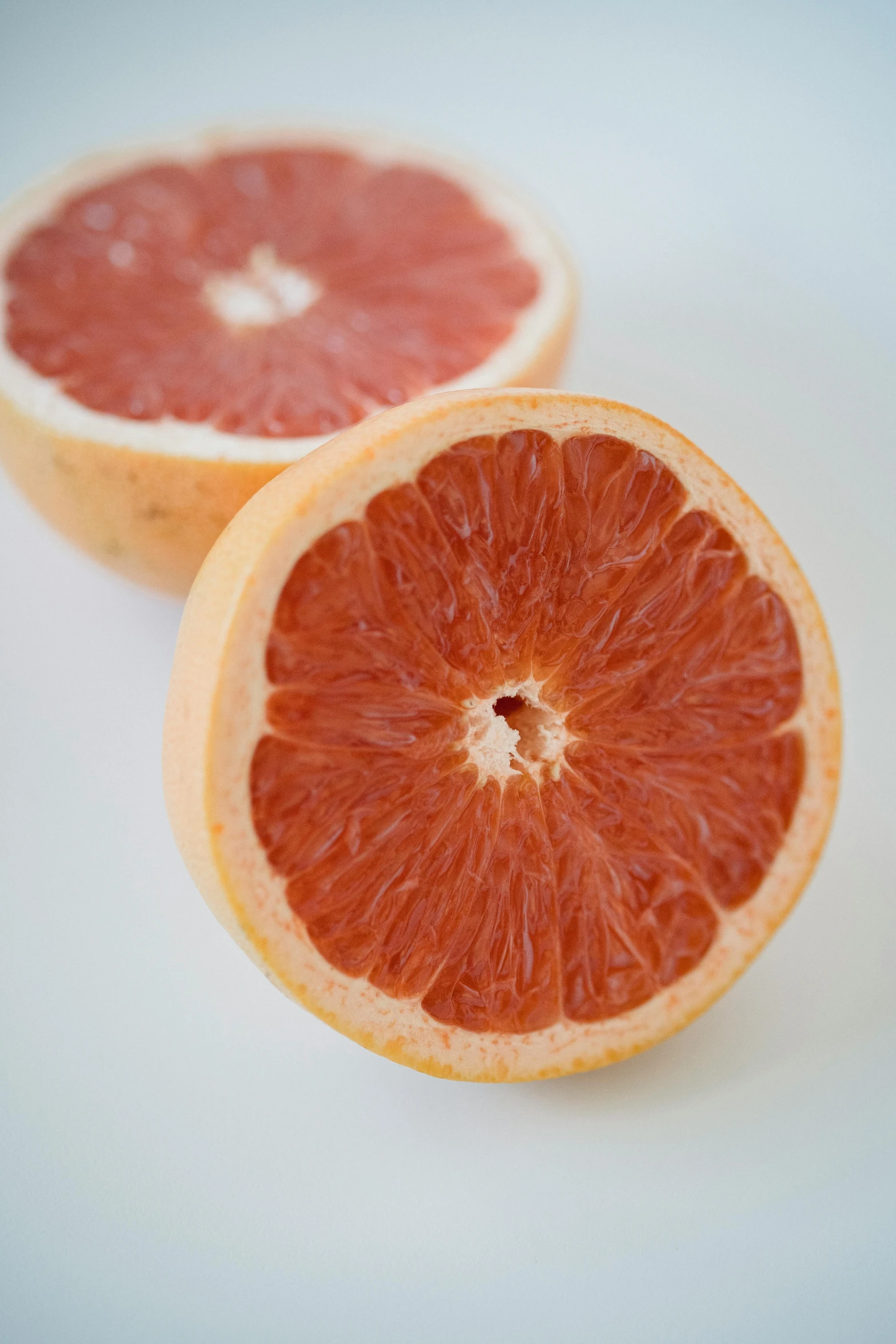 two grapefruits cut in half on a white surface, by Julian Allen, unsplash, made of glazed, detailed and soft, alabama, bottom body close up