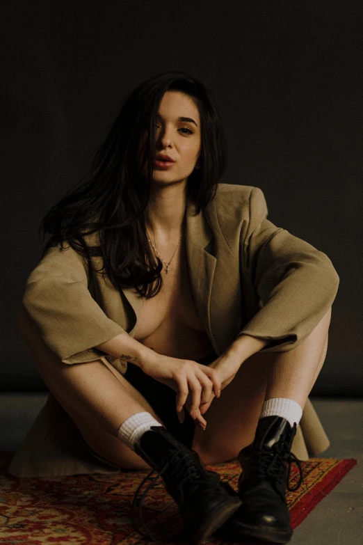 a beautiful young woman sitting on top of a rug, by Sebastian Vrancx, reddit, wearing a worn out brown suit, yael shelbia, jacket over bare torso, promo image