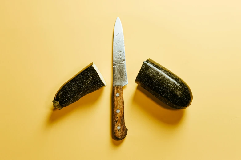 two zucchini and a knife on a yellow surface, a still life, by Carey Morris, unsplash, renaissance, with a wooden stuff, detailed product image, holding a kitchen knife, on clear background