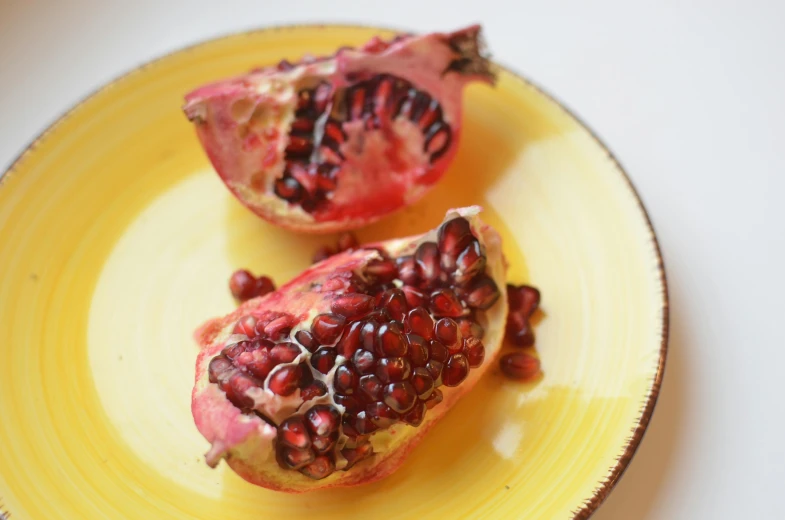 two pieces of pomegranate on a yellow plate, by Carey Morris, pexels, on a pale background, skin, unedited, jen yoon