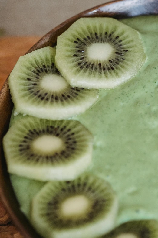 a bowl filled with kiwi slices on top of a wooden table, inspired by Kanō Tan'yū, hurufiyya, seafoam green, bottom body close up, cake, close-up from above