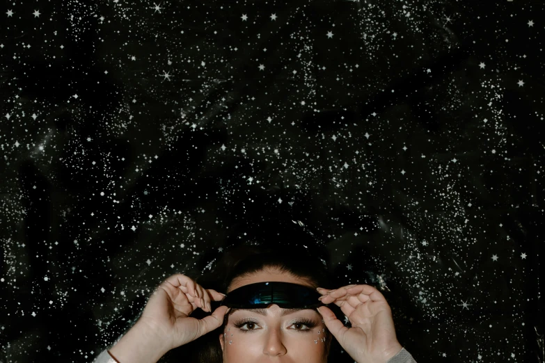 a woman covering her eyes with a pair of blindfolds, by Julia Pishtar, trending on pexels, magical realism, stars in space, wearing a headband, top down view, portrait photo of a backdrop