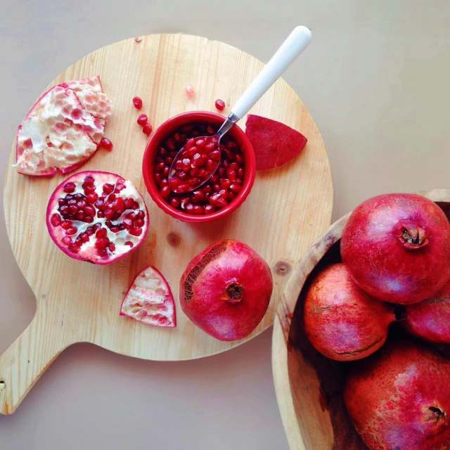 a wooden cutting board topped with pomegranates, by Niko Henrichon, pexels, bowl filled with food, creamy, magenta colours, red color theme