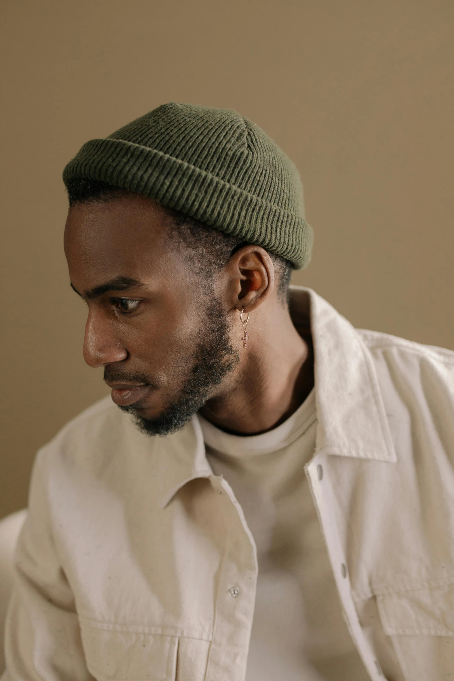 a man sitting on a couch wearing a hat, a character portrait, inspired by Barthélemy Menn, trending on pexels, jaylen brown, side profile waist up portrait, olive green, beanie