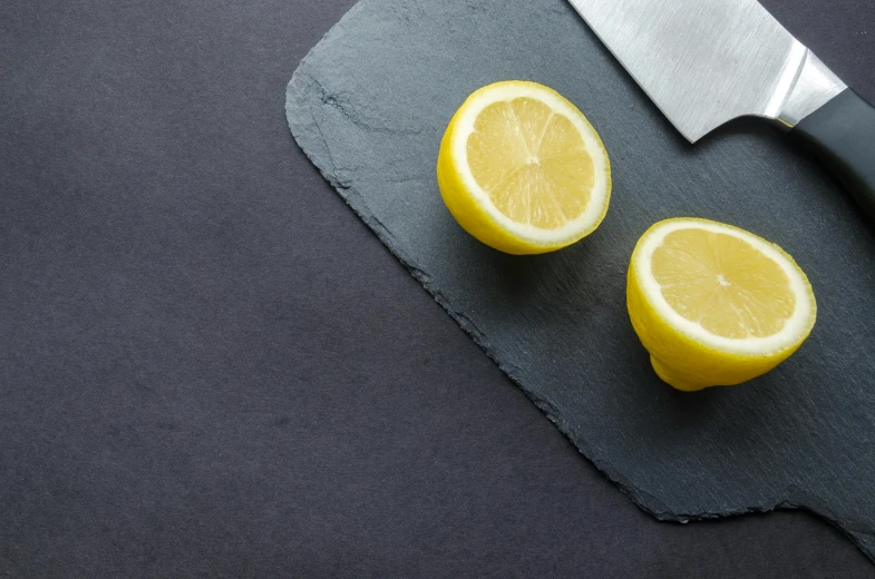 a knife sitting on top of a cutting board next to two lemons, inspired by Grillo Demo, trending on unsplash, minimalism, slate, background image, thin porcelain, thumbnail