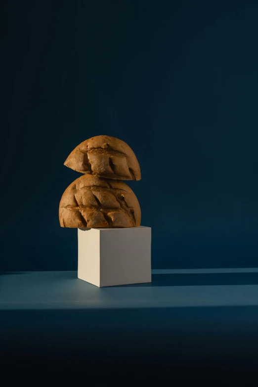 a pile of bread sitting on top of a white box, an abstract sculpture, inspired by Isamu Noguchi, unsplash, profile portrait, with a blue background, dramatic product lighting, pastry