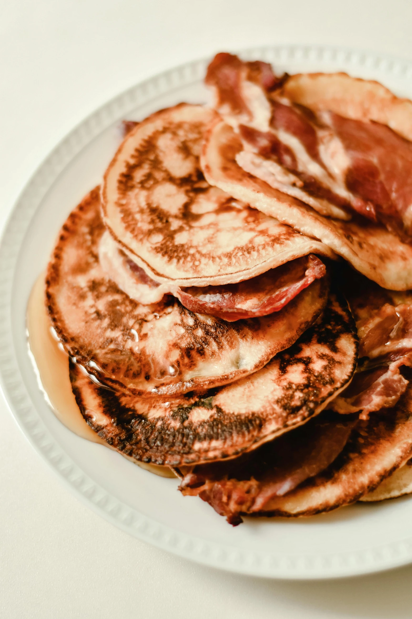 a white plate topped with pancakes covered in bacon, by Winona Nelson, pexels, piled around, sunfaded, made of glazed, thumbnail