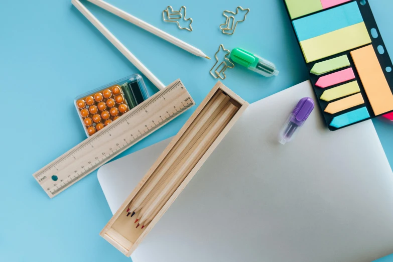 a laptop computer sitting on top of a desk, a still life, trending on pexels, academic art, children drawing with pencils, chartreuse and orange and cyan, wooden art toys on base, blue and purple colour scheme