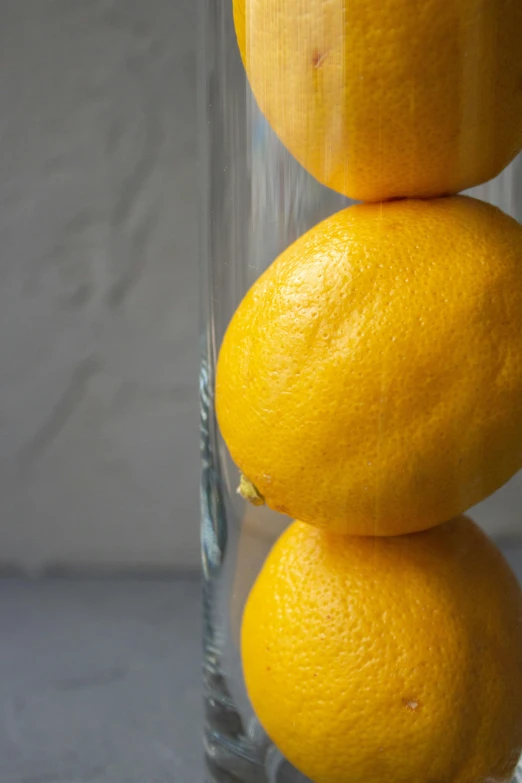 three oranges stacked on top of each other in a glass, a still life, unsplash, lemon demon, close up shot from the side, tall thin frame, a long-shot from front